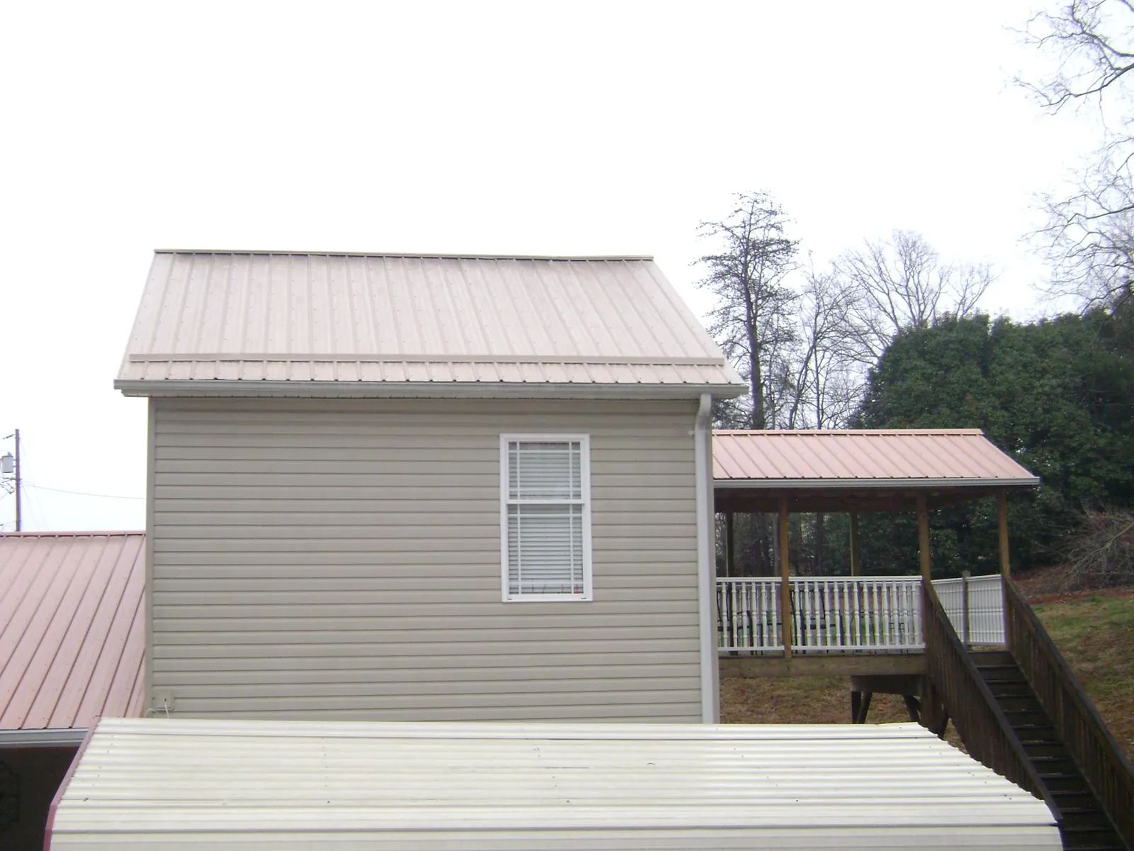 Tan metal roofs on a two story addition and attached porch, from a Roof Replacement job in Walton